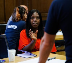 A photo of a dark haired woman in a red top engaged in conversation