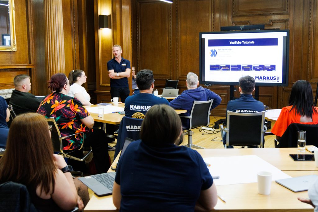 A photo showing nine people looking at a screen with a man in blue talking to them to the left of the screen