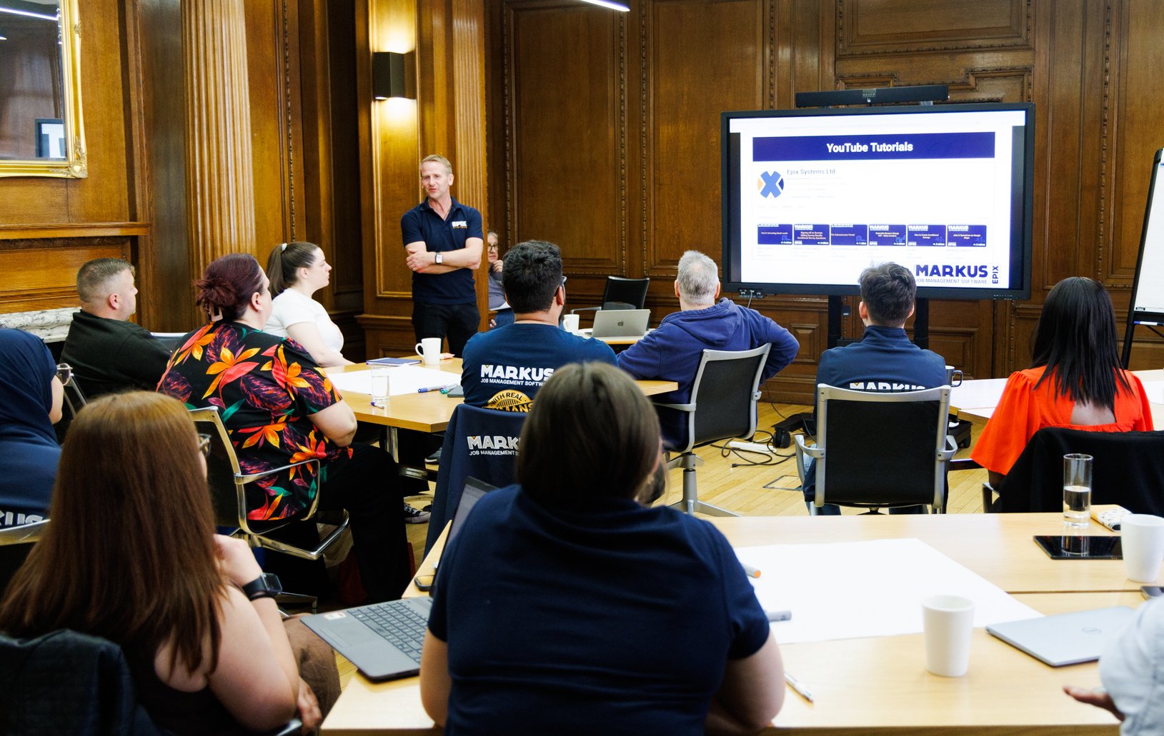 A photo showing nine people looking at a screen with a man in blue talking to them to the left of the screen