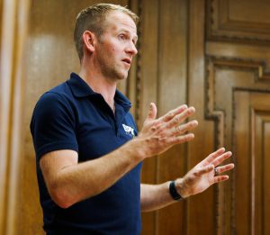 A photo of a light haired man in a blue polo shirt giving a talk