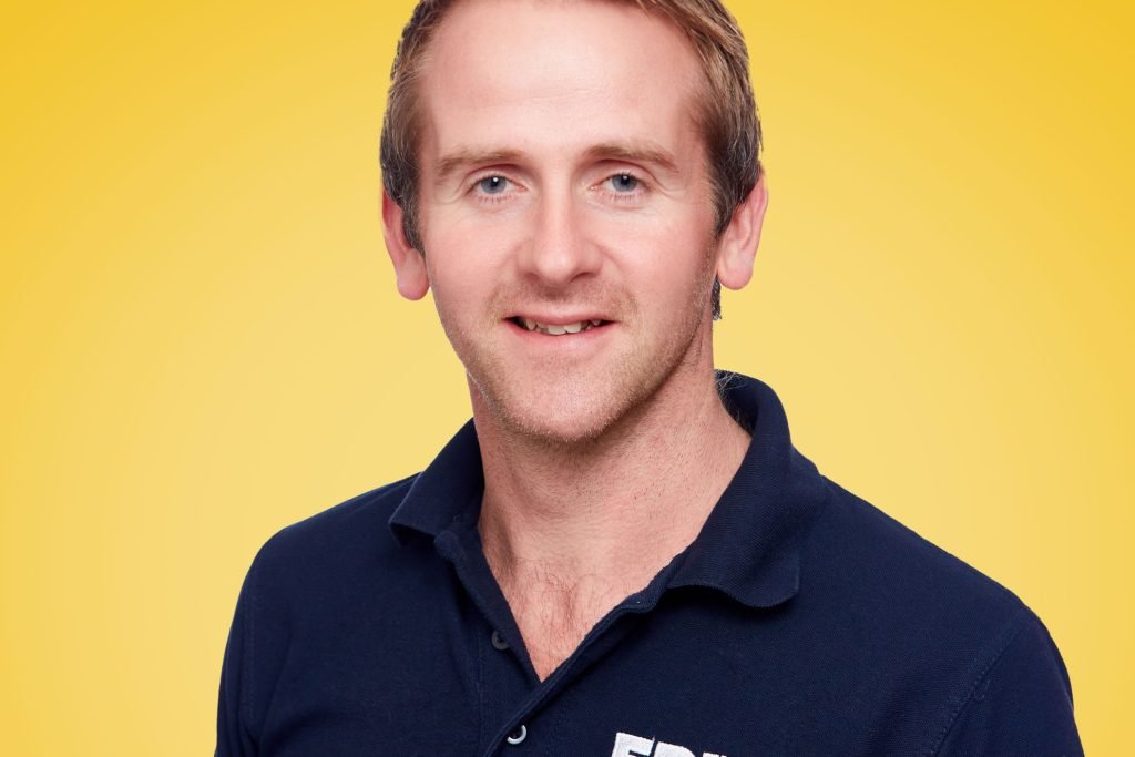 A photo of Chris, in a blue EPIX shirt against a yellow background