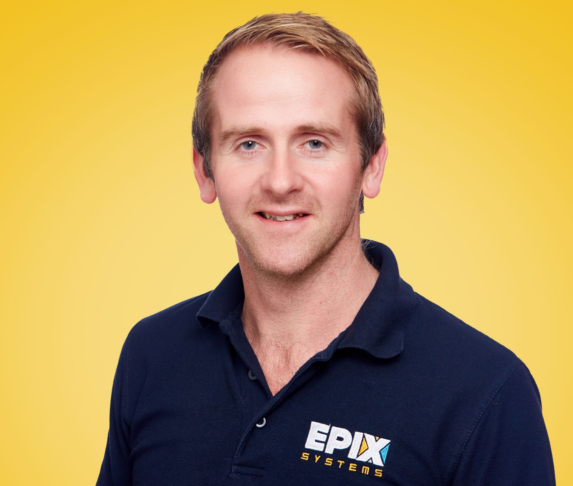 A photo of Chris, in a blue EPIX shirt against a yellow background